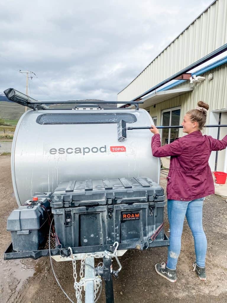 A woman using a soap scrubbing brush to scrub down her teardrop camper.