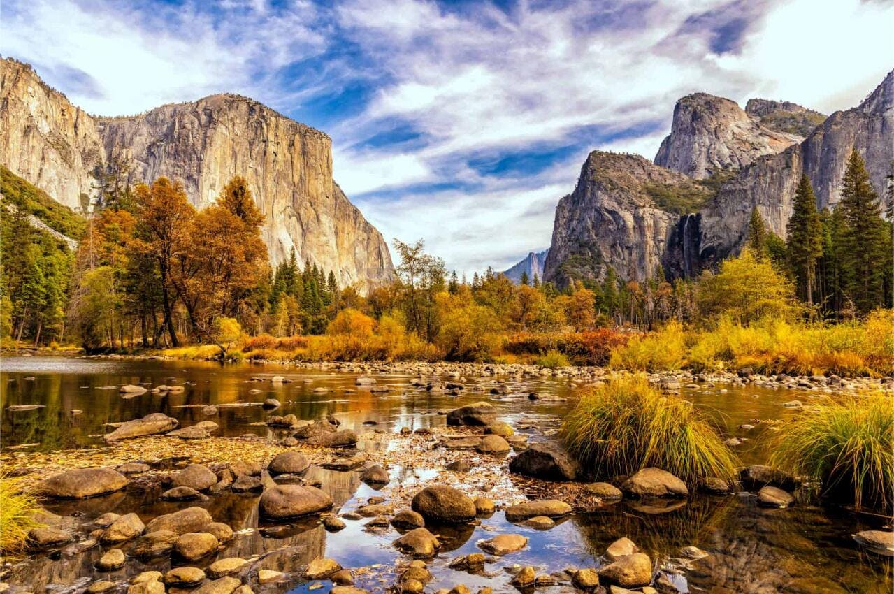 Sheer rock cliffs tower behind a stream in Yosemite during the fall.