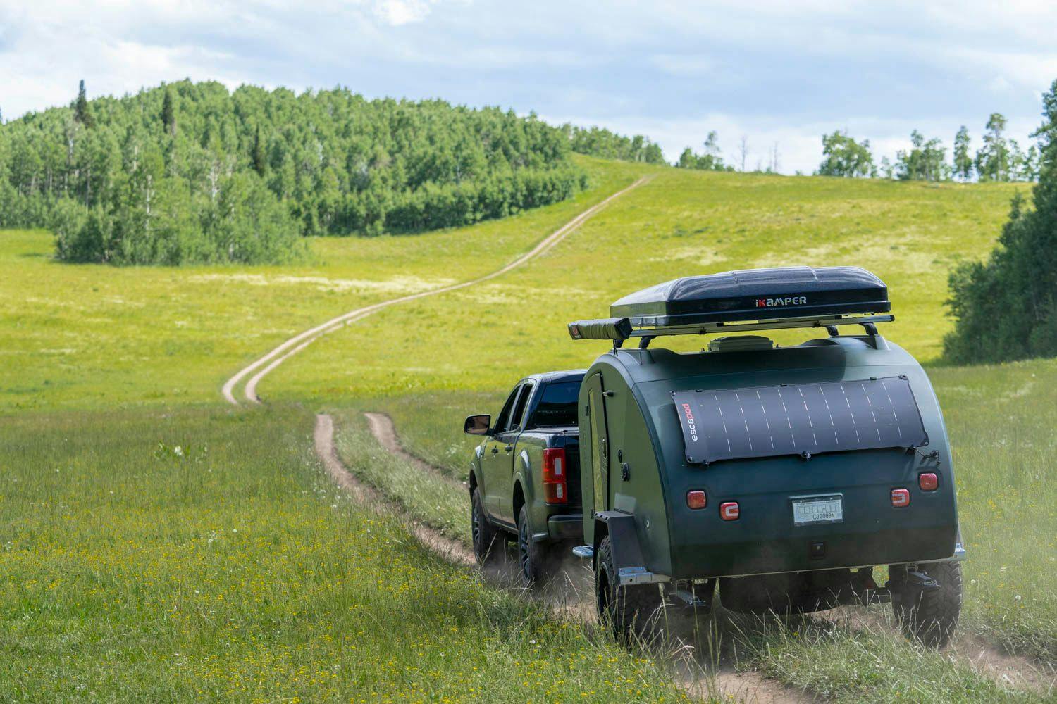 A teardrop camper being towed up a mountainside with a rooftop tent on top.