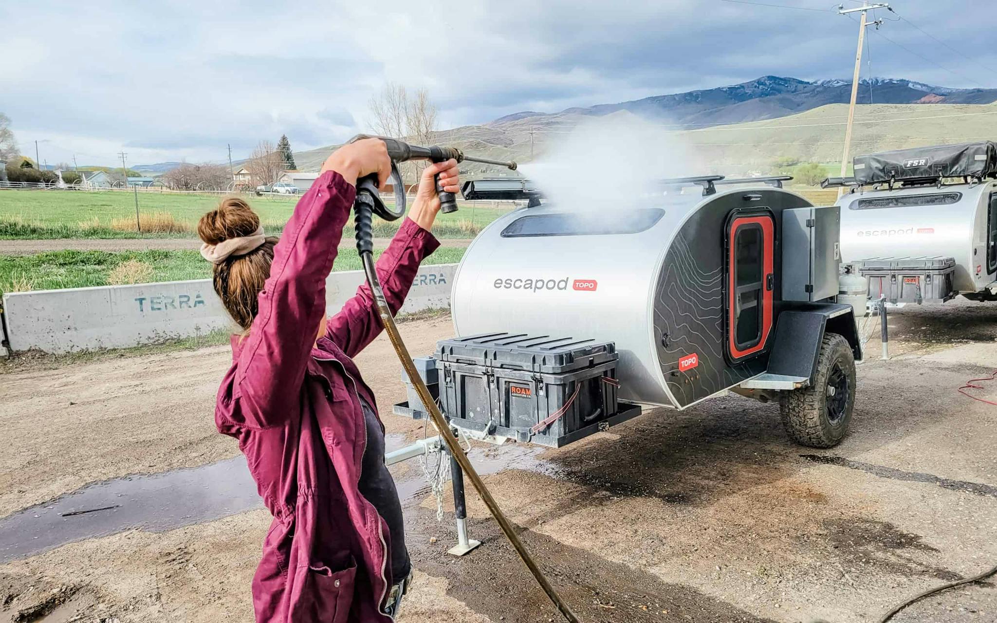 A woman using a hose attachment to spray off her teardrop trailer.