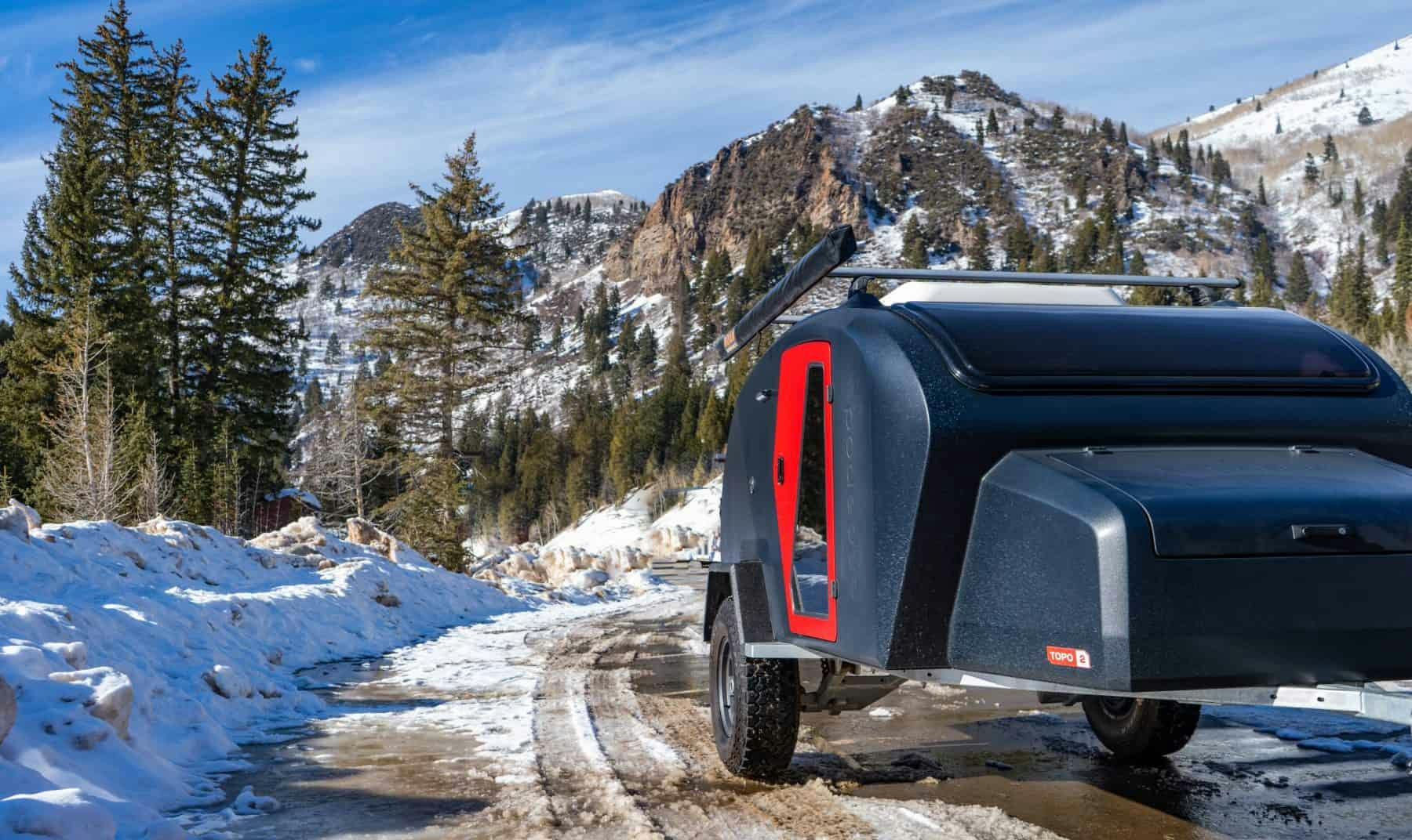 A navy teardrop camper pulled off the side of the road with winter landscape behind it.