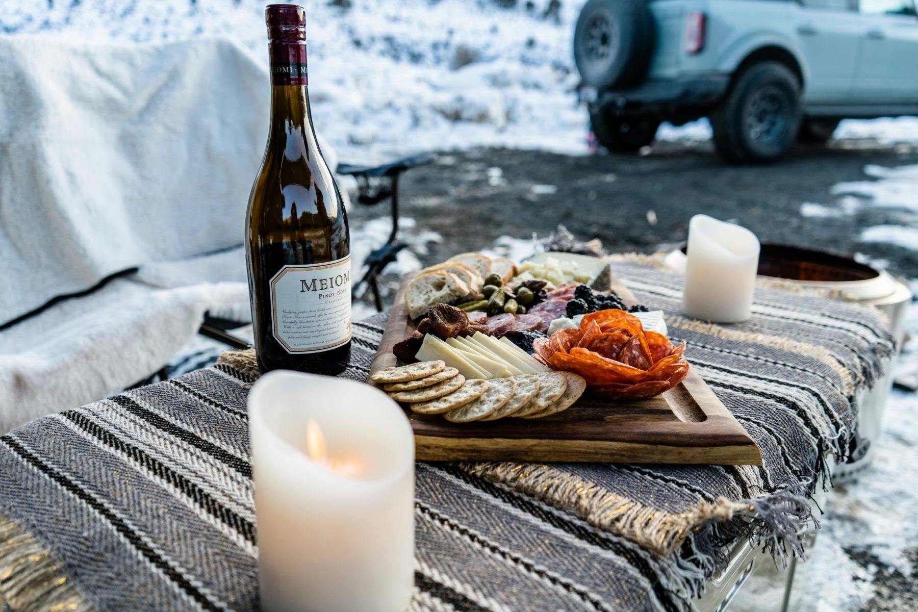 A charcuterie board and wine set up outside of trailer that is being towed by a Ford Bronco.