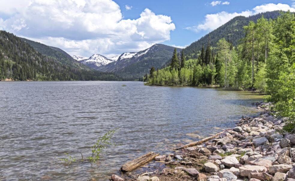 A beautiful lake surround by pine trees, mountains, and blue skies.