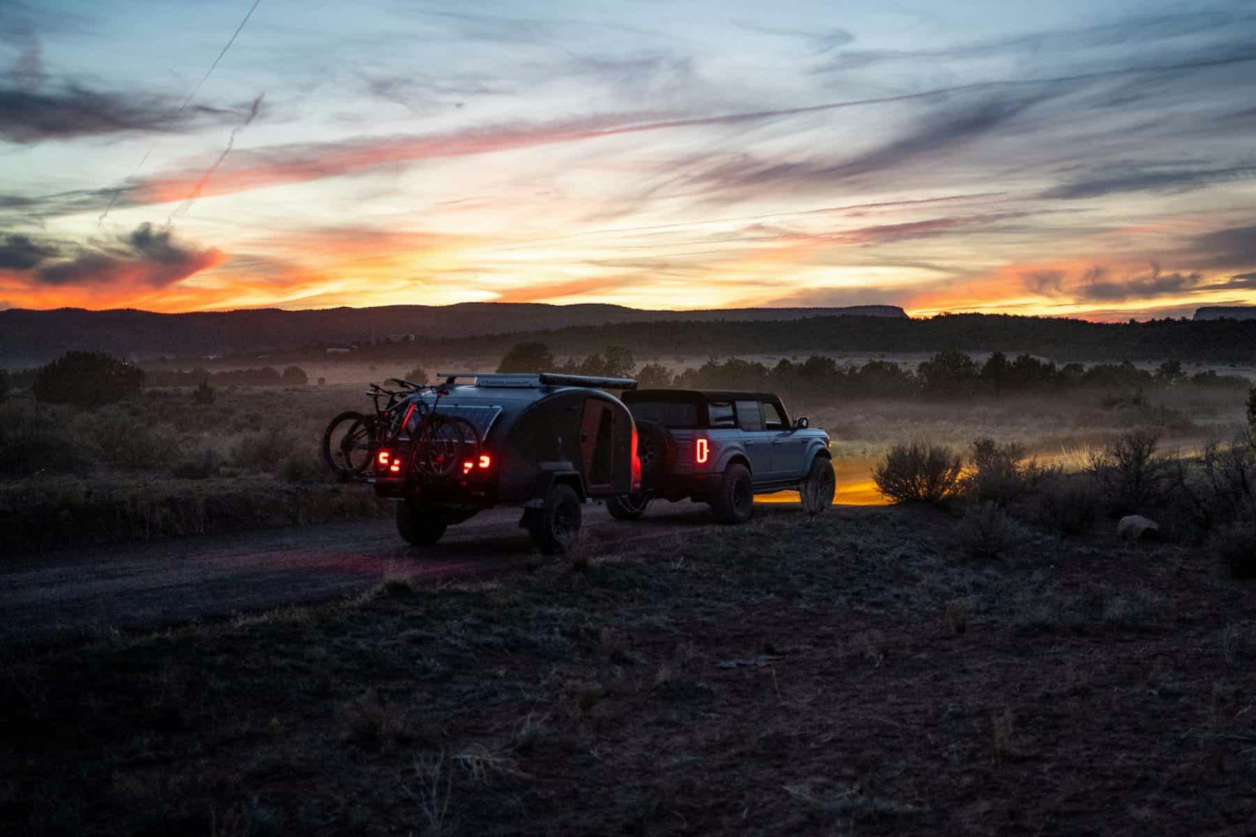 A navy blue teardrop camper being towed through desert landscape by a Ford Bronco.