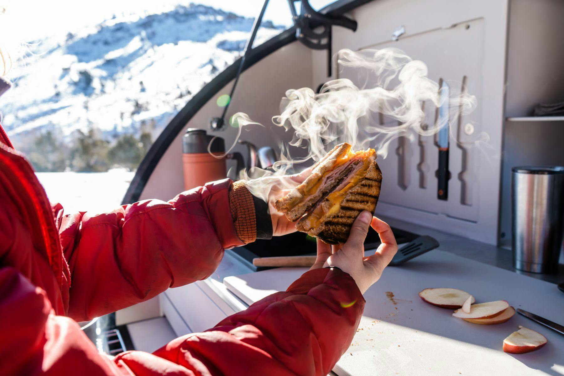 A panini sandwich being split in half in a the galley of a teardrop camper.