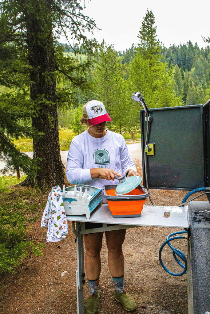 A woman washing dishes outside her teardrop camper.