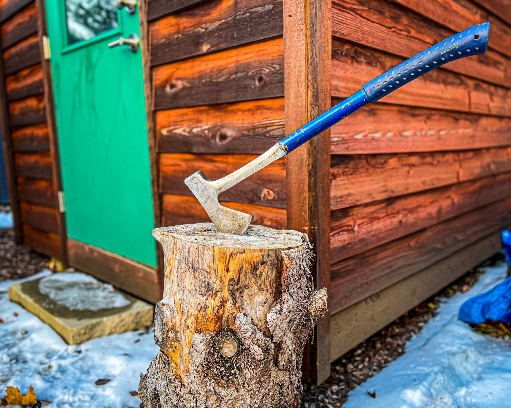 A photo of a splitting axe, in a log.