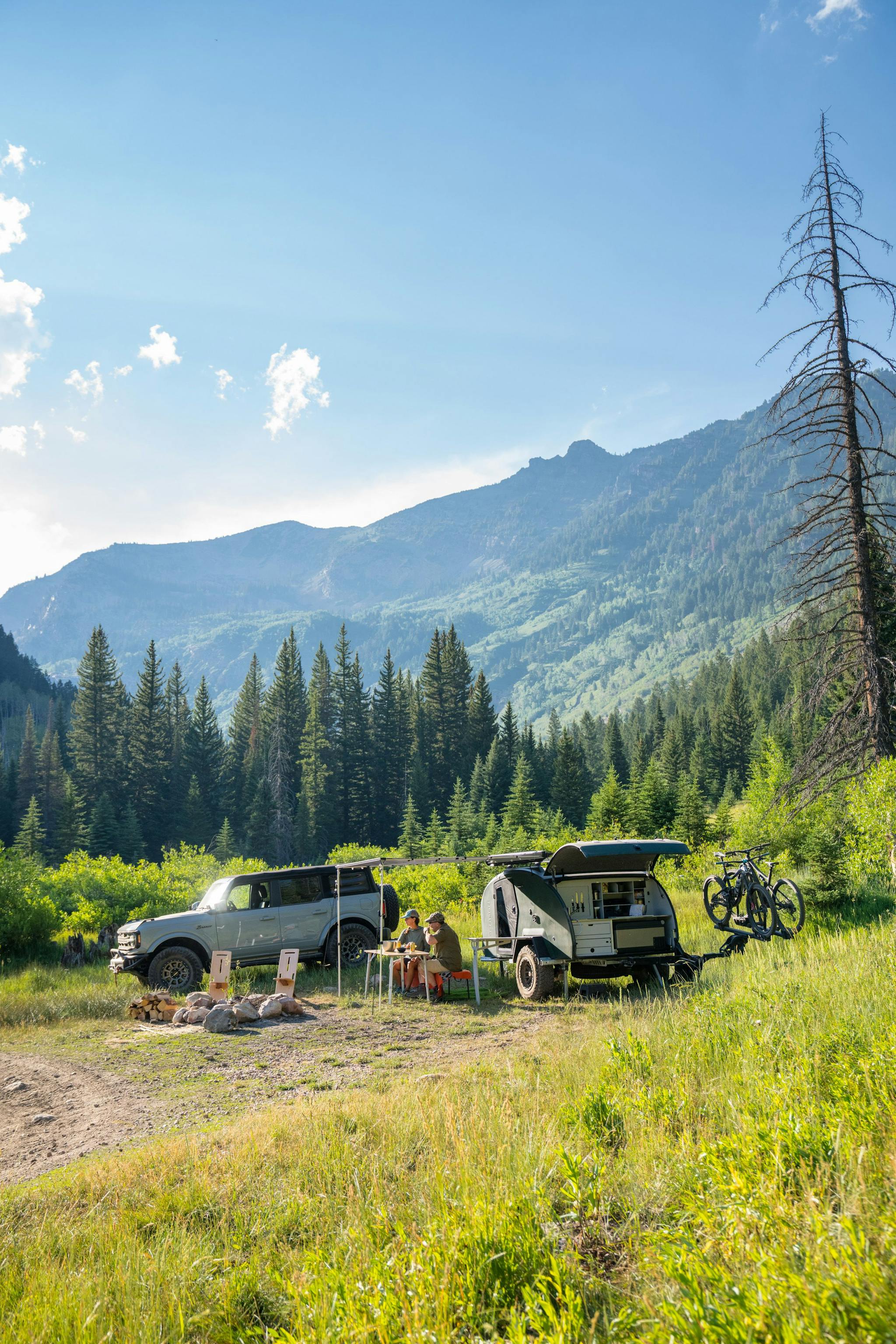 A teardrop trailer set up in a beautiful green field, surrounded by trees and blue skies.