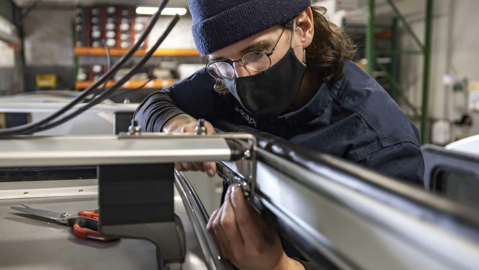 A craftsperson working to install a ROAM Adventure awning onto a teardrop trailer build.