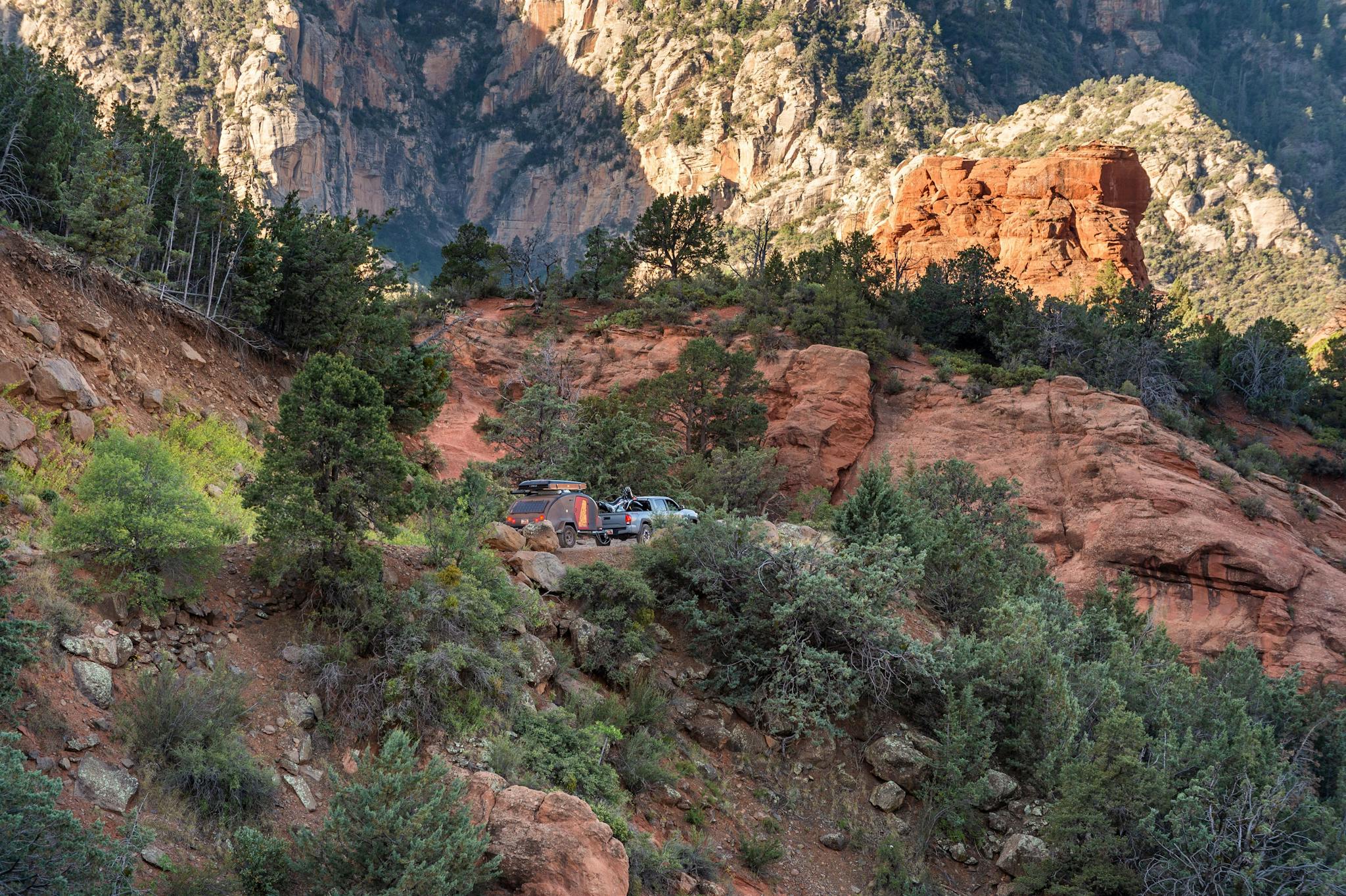 A navy blue teardrop camper being towed through desert landscape by a Ford Bronco.