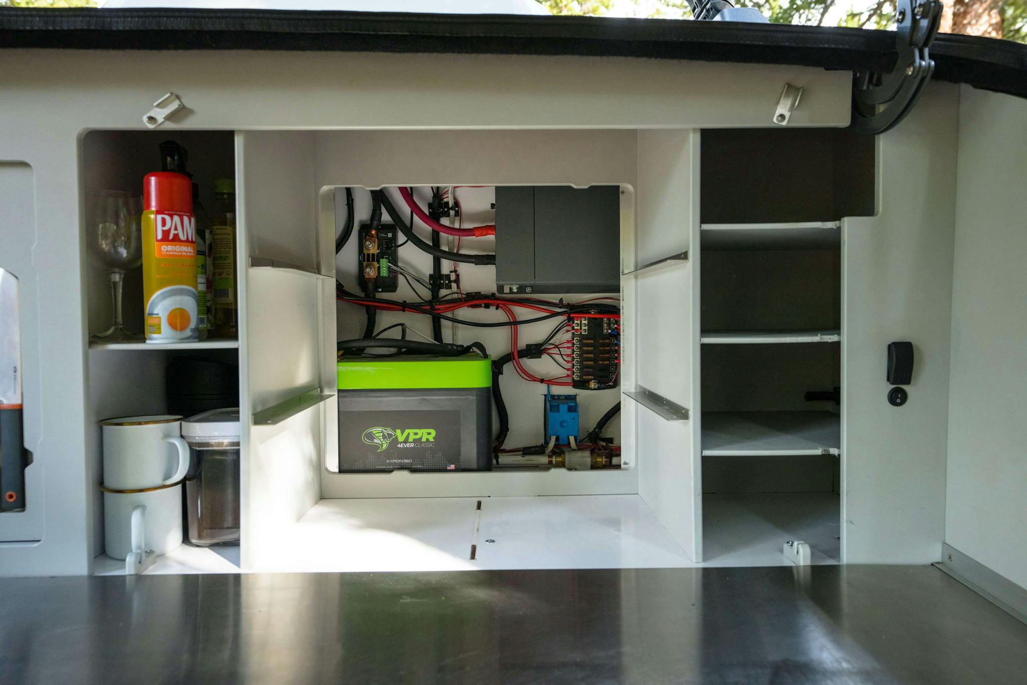 Behind the modular shelving in a teardrop trailer galley a battery setup with a lithium battery to power the trailer.