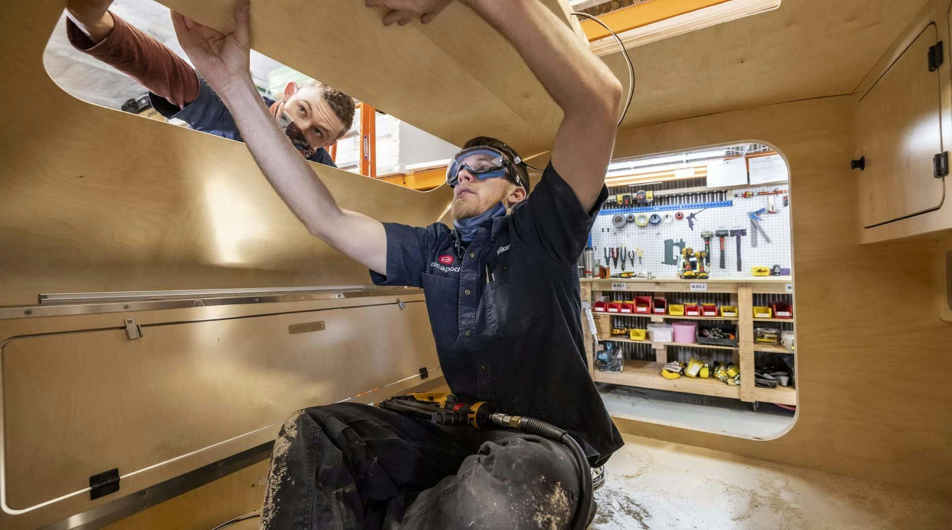 Multiple craftspeople working to install the interior roof of a teardrop camper in a small manufacturing facility.