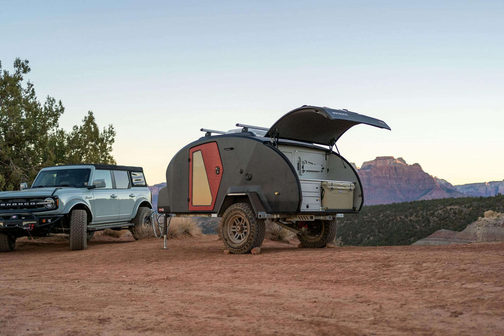 A navy blue teardrop camper with a red door, parked next to a Ford Bronco at Gooseberry Mesa.