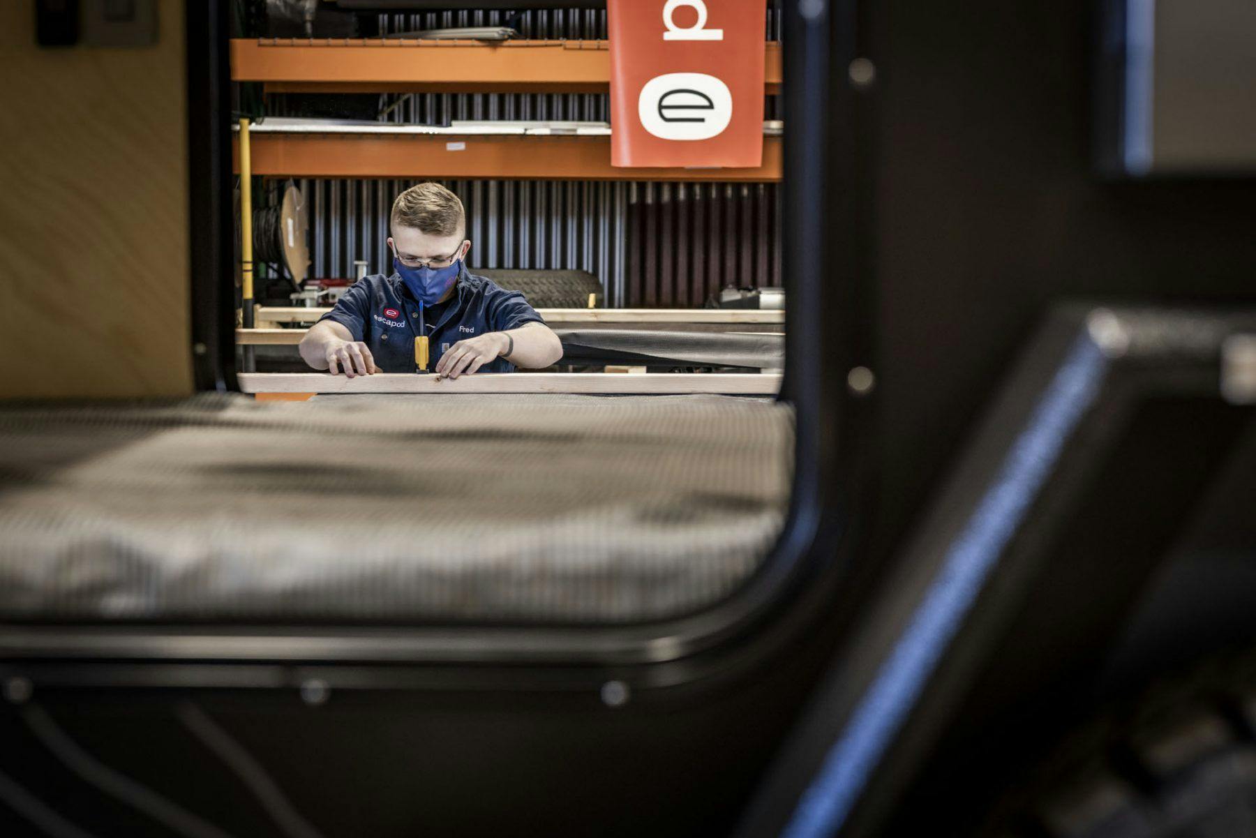 A craftsman working on building a teardrop camper in a small manufacturing shop.