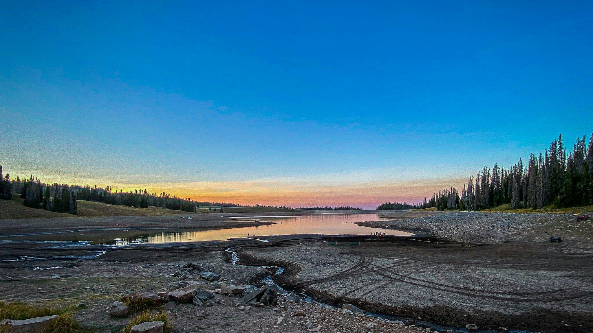 Glassy water at Whitney Reservoir in Utah is reflecting a glowing night sky at sunset.