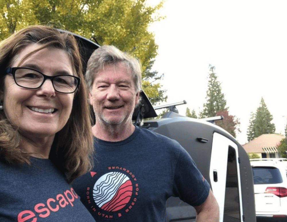 A couple in navy blue t-shirts in front of their TOPO2, an offroad adventure trailer.