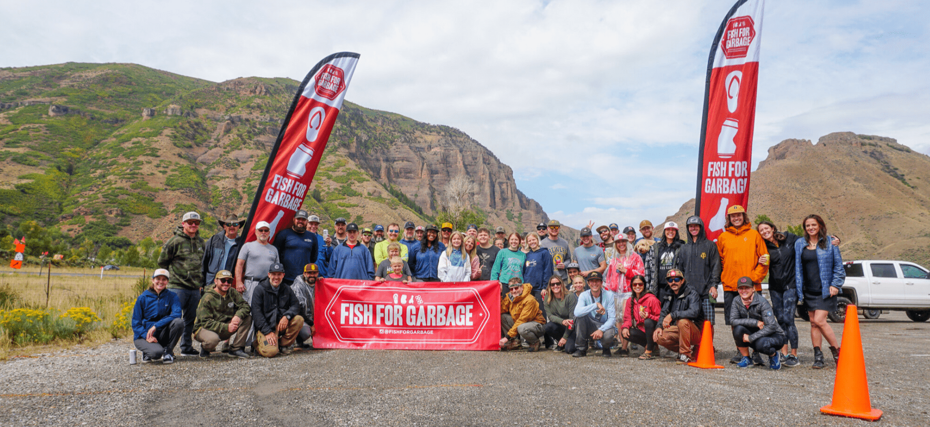 A team is standing in front of a banner for Fish for Garbage, where Escapod employees team up with Fish for Garbage to clean the Weber River.