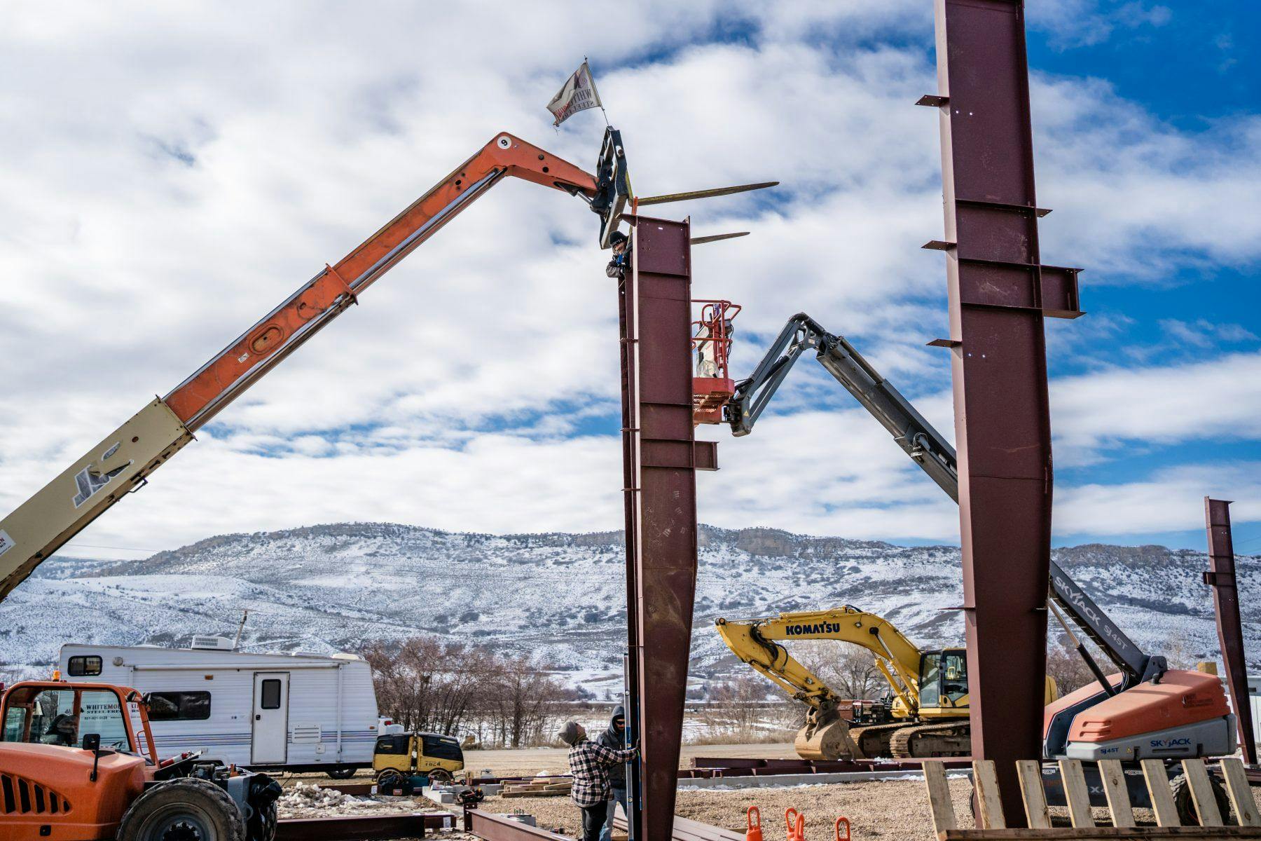 A blue sky winter day, with structural beams being set up to build a new manufacturing space with a crane.