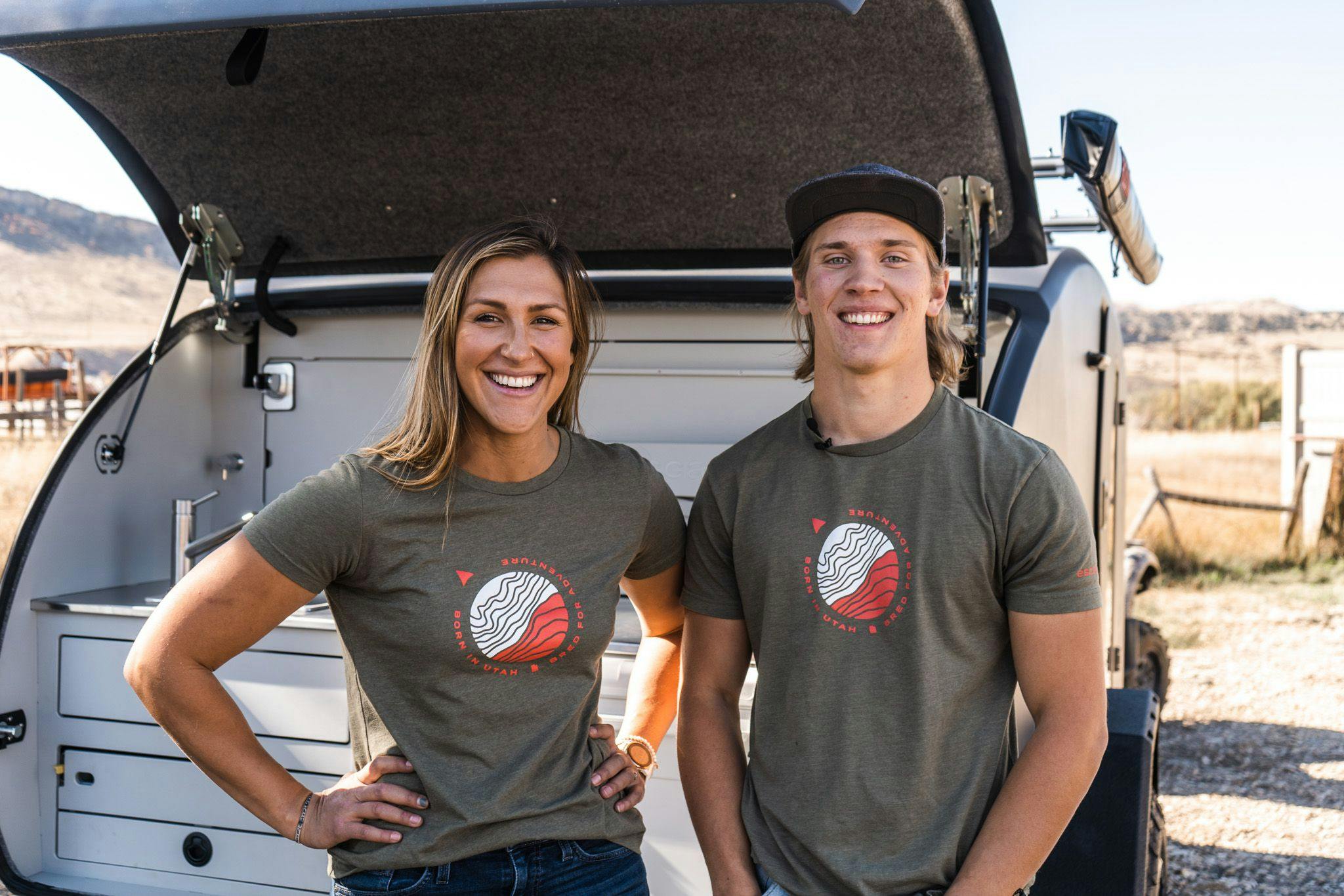 Picture of two people smiling in front of an adventuer trailer.