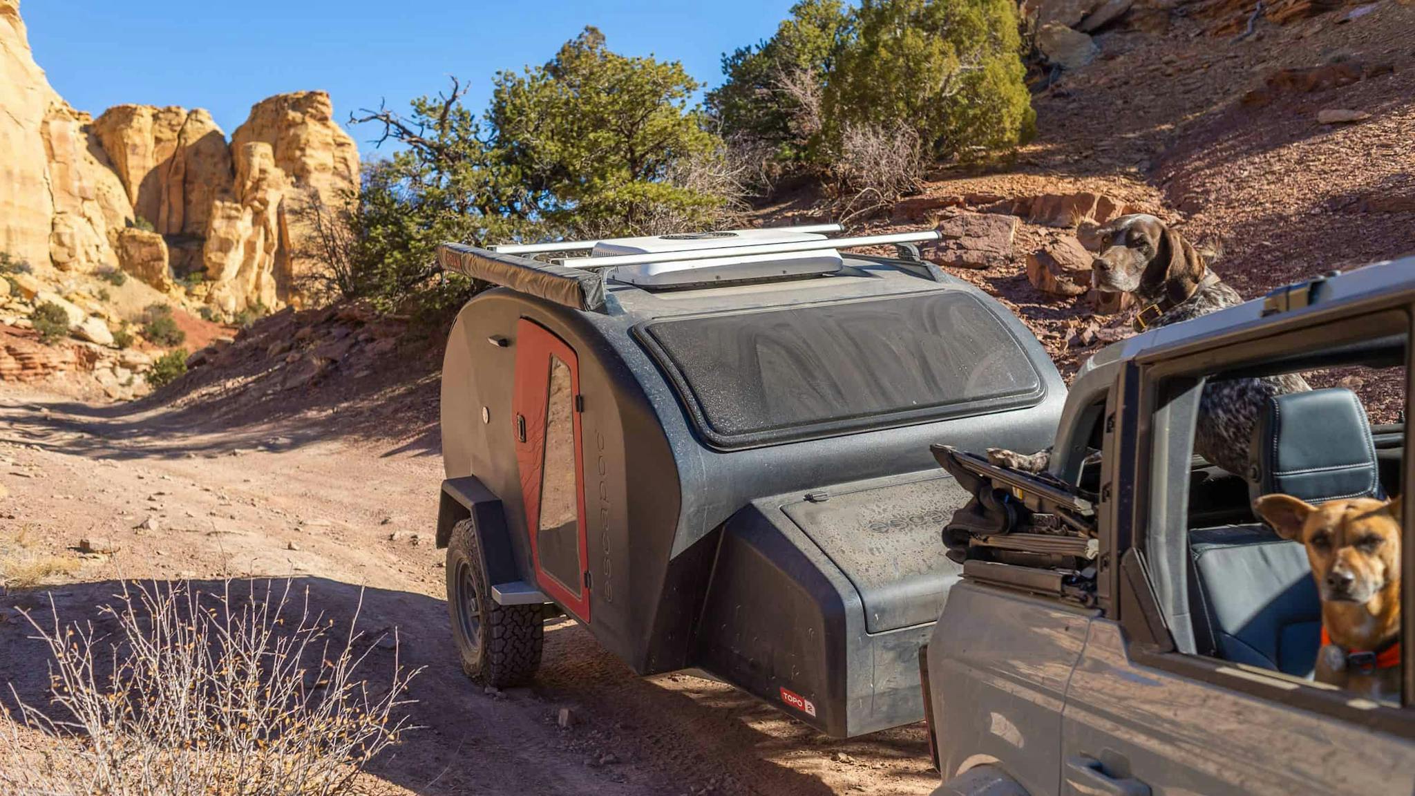 A navy blue teardrop camper being towed through desert landscape by a Ford Bronco.