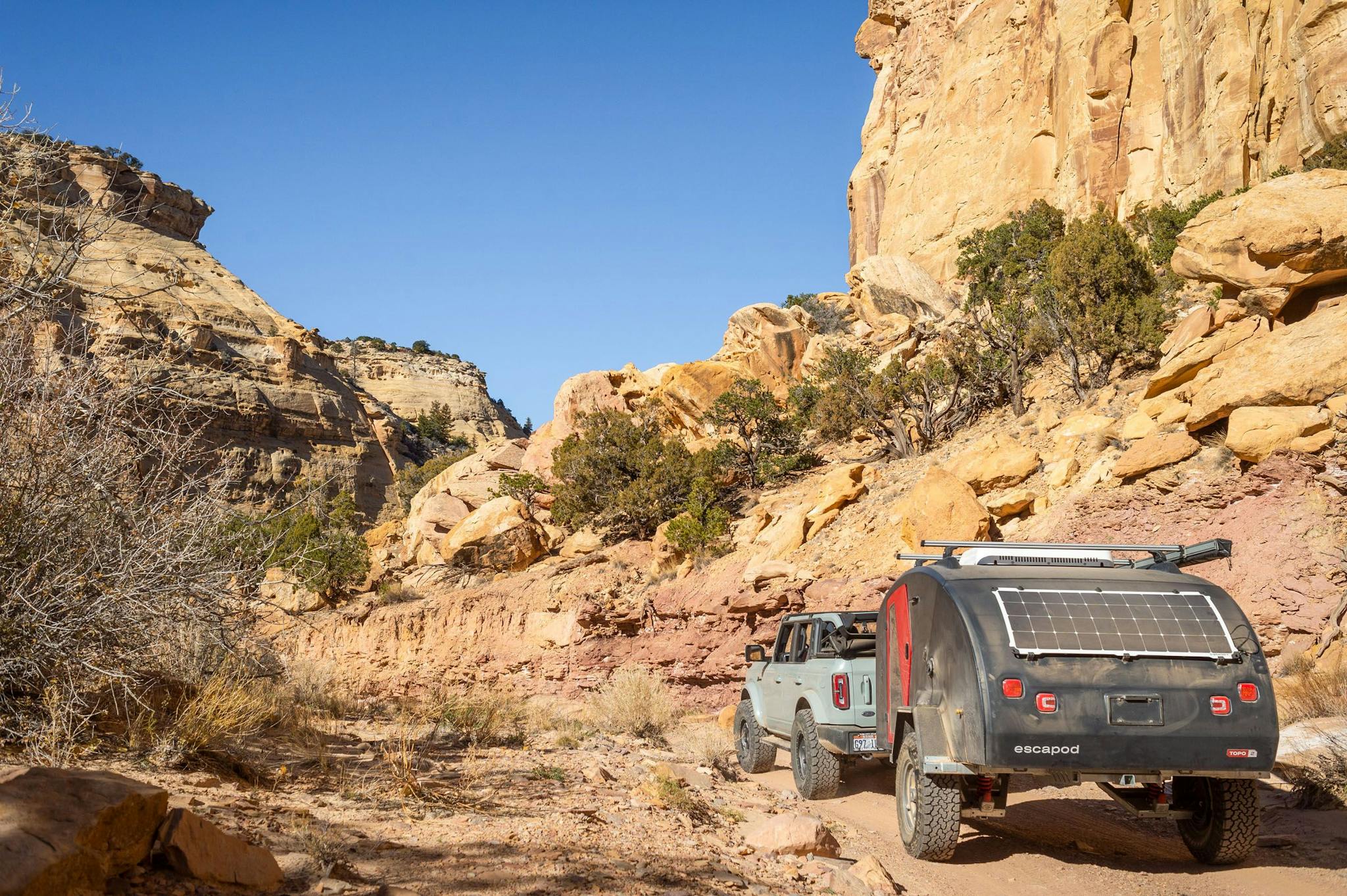 A navy blue teardrop camper being towed through desert landscape by a Ford Bronco.