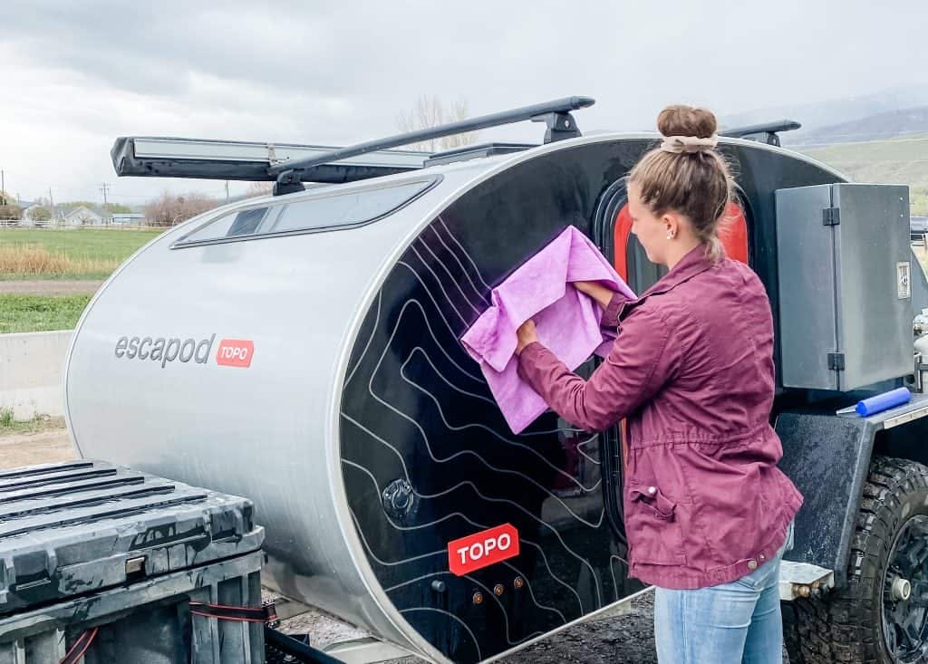 A woman using a purple towel to wipe down the exterior of her black and red teardrop camper.