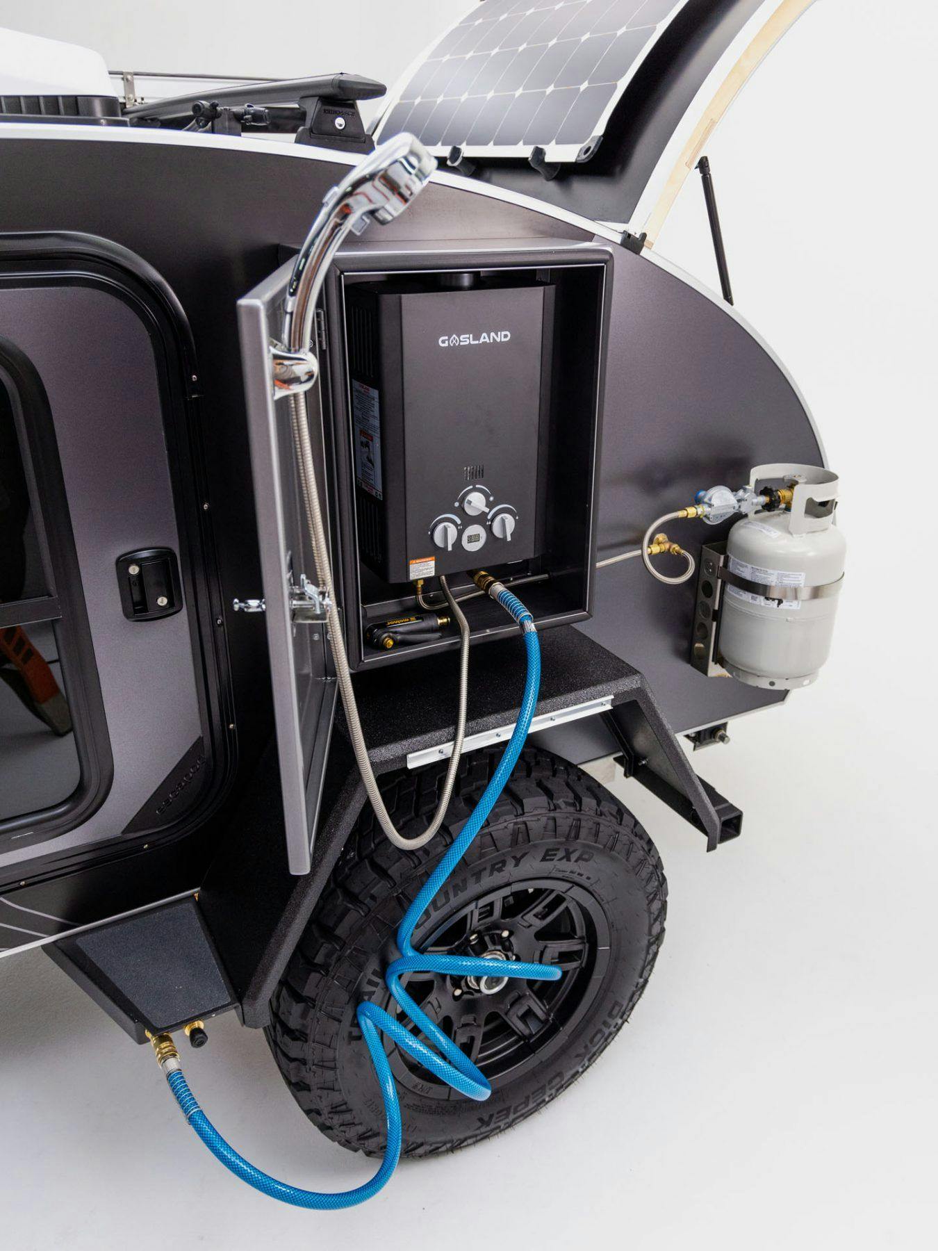 A hot water heater/shower mounted on the exterior of a black and grey offroad trailer.