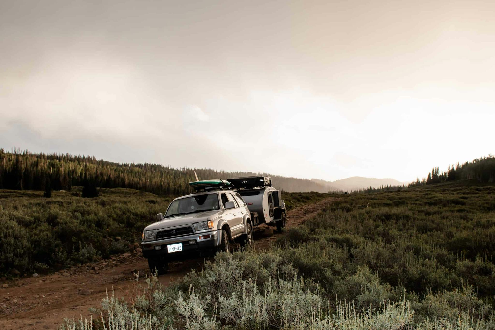 A teardrop trailer being towed by a grey Toyota through a sagebrush terrain.