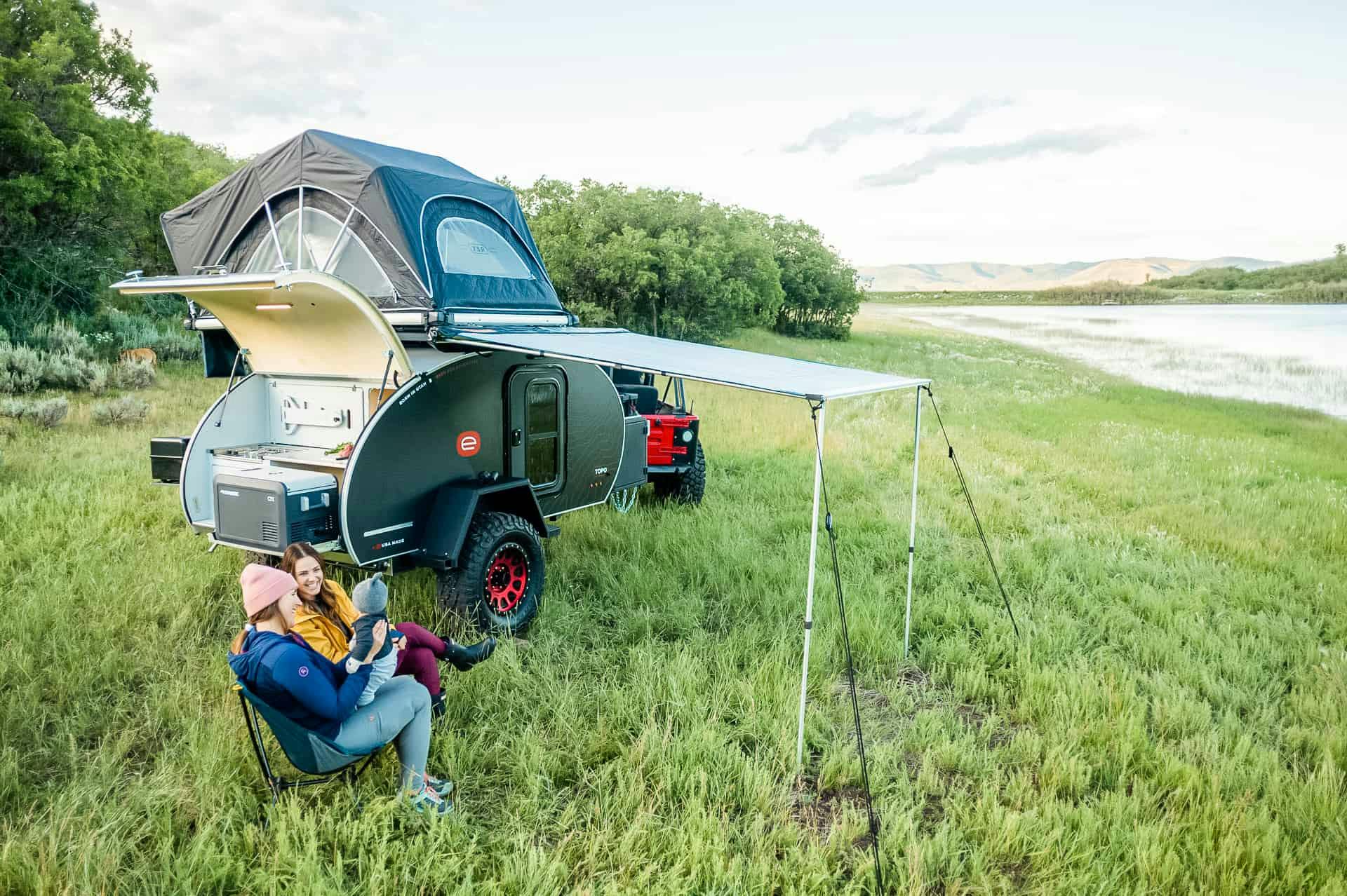 Two women and a small child enjoying their campsite next to a teardrop camper.