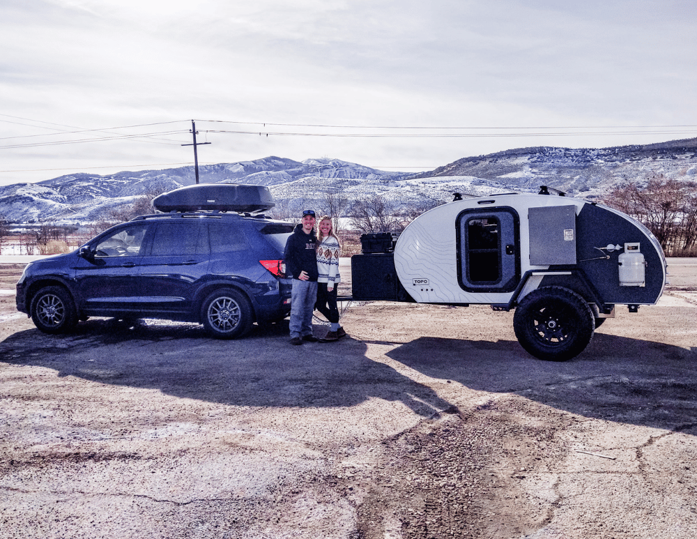 A grey and white Original TOPO trailer being picked up by a happy couple.