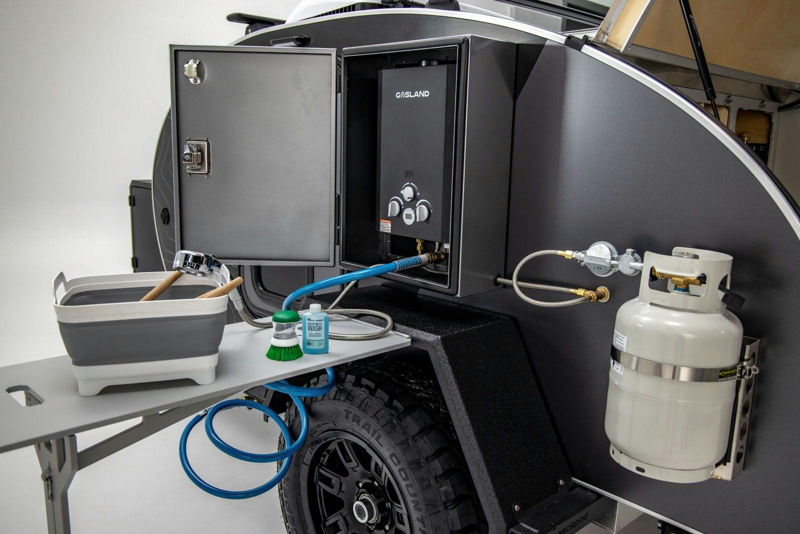 A hot water heater/shower mounted on the exterior of a black and grey offroad trailer.