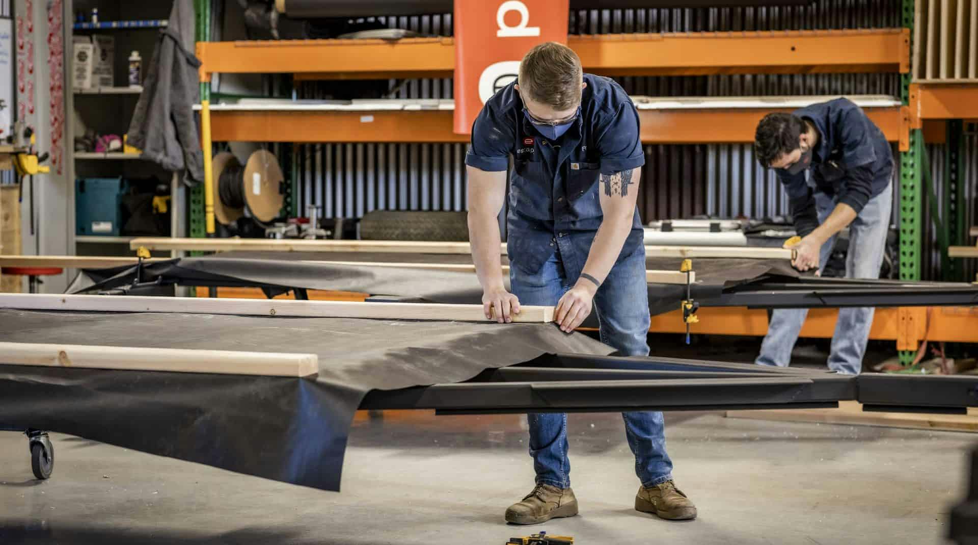 Multiple craftspeople laying the underliner fabric onto the frame for a teardrop trailer build.