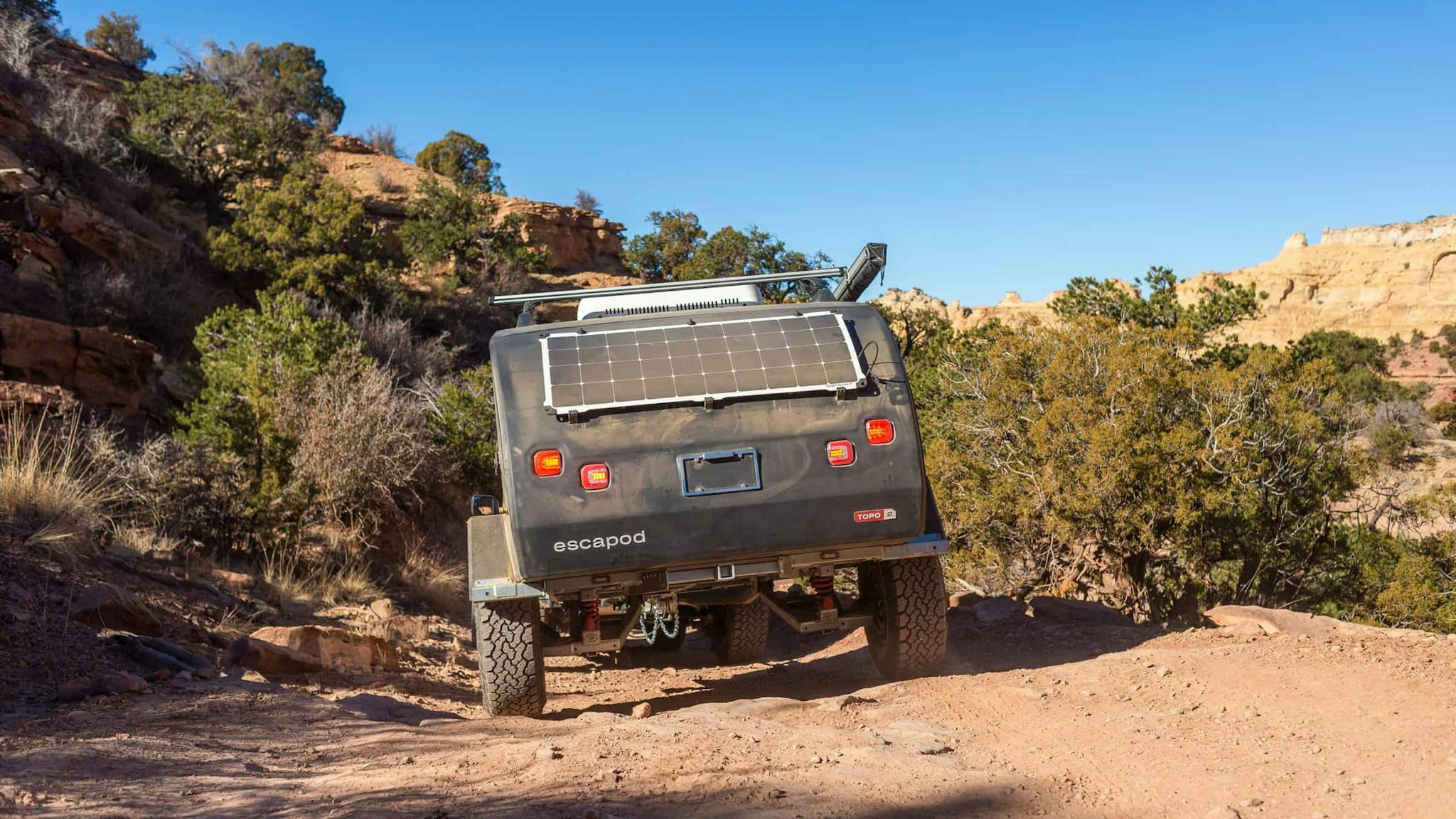 A navy blue teardrop camper being towed through desert landscape by a Ford Bronco.