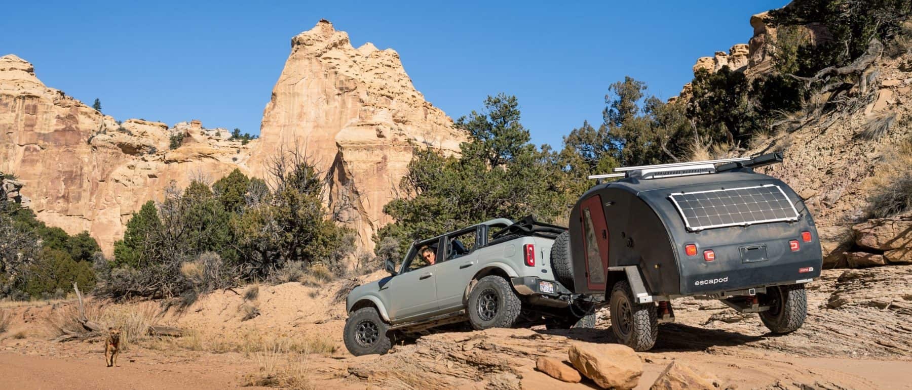 A navy blue teardrop camper being towed through desert landscape by a Ford Bronco.