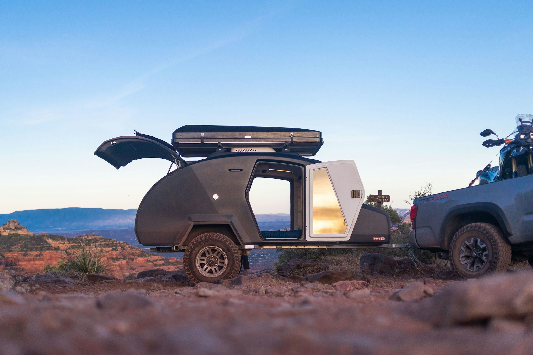 A TOPO2 teardrop camper sits atop Schnebly Hill above Sedona, Arizona at dawn. The doors are open revealing the city below.